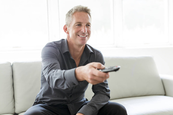 Portrait of single 40s man sitting in sofa tv remote - Photo, image