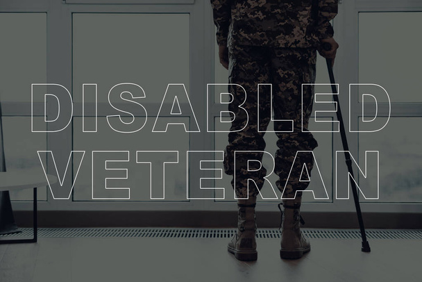 Military Veteran. Man Standing in Front of Window. Large Panoramic Window. Man with Crutch. Man is Soldier. Soldier in Military Uniform. Man Looking into Window. Man Located in the Living Room. - Foto, Bild