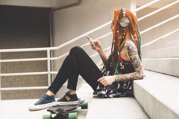 young girl with tattoo and dreadlocks listening to music while sitting on the steps - Fotografie, Obrázek
