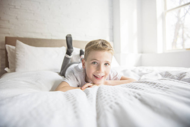 Beautiful caucasian boy on a sunny morning in a white bed. - 写真・画像