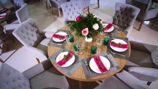 een ronde houten tafel versierd met bloemstukken gemaakt van witte platen met roze servetten rond die er zachte stoelen zijn - Video