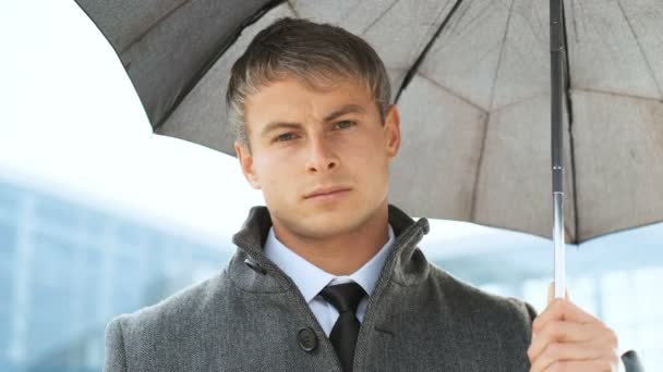 Close up portrait of man under black umbrella during rain. Serious businessman wearing suit and coat, looking at camera. - Filmati, video