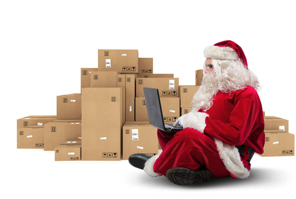 Technologiczne Santa Claus siedząca z laptopem kupuje prezenty świąteczne z e-commerce - Zdjęcie, obraz