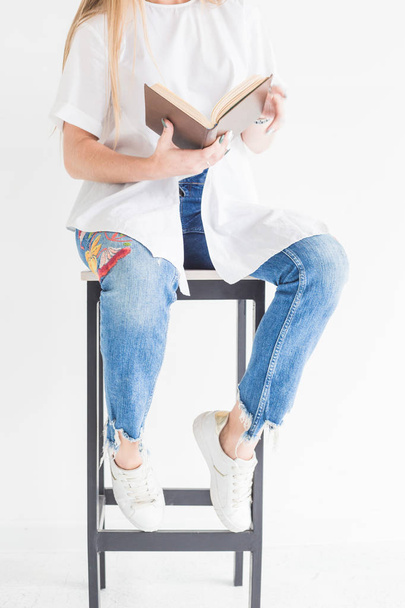 Nuoren tyylikkään vaalean tytön muotokuva valkoisessa t-paidassa ja sinisissä farkuissa lukemassa kirjaa valkoisella taustalla
 - Valokuva, kuva