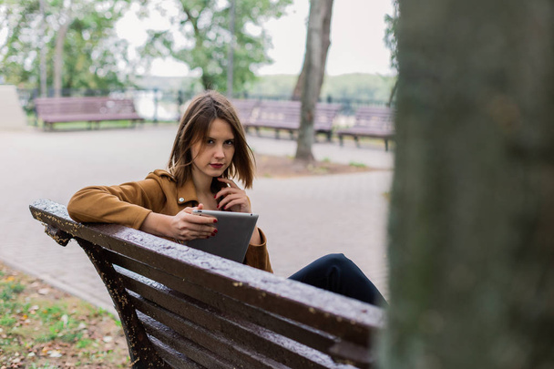 Krásná dívka sedí na lavičce s tabletem v parku. - Fotografie, Obrázek