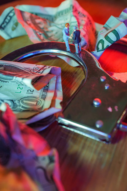 Konceptuální miniaturní kriminální podnikatelé potřást rukou panenka pouta s zmačkaný dolarové bankovky a policejní světla - Fotografie, Obrázek