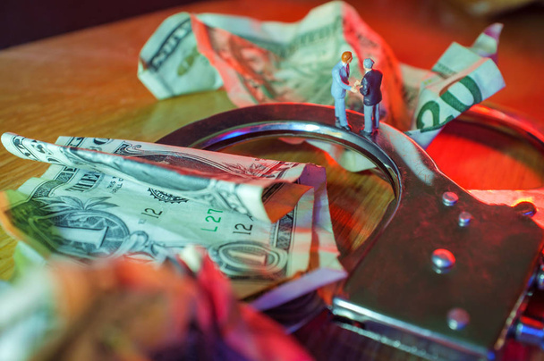 Konceptuální miniaturní kriminální podnikatelé potřást rukou panenka pouta s zmačkaný dolarové bankovky a policejní světla - Fotografie, Obrázek