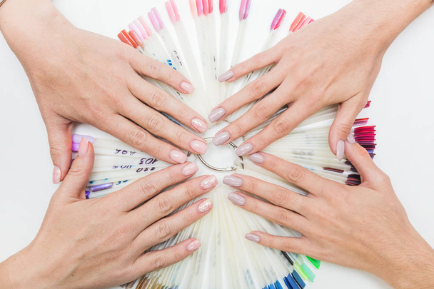 Top view of beautiful womans hands with collection of color nail polish samples on white background - Photo, Image