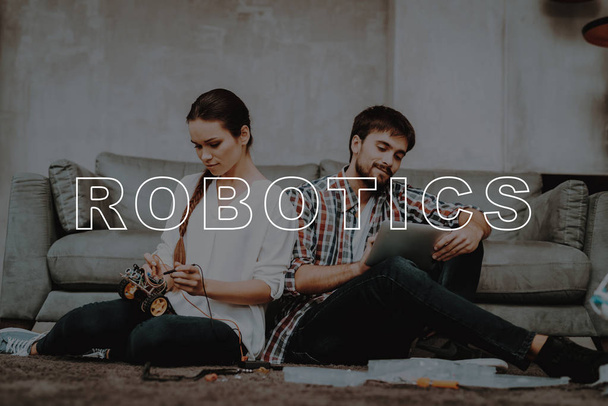 Young Couple. Sit. Floor. Living Room. Collect. Robots. Guy. Tablet. Work Together. Help. Girl. Smiling. Beautiful. Happy. Leisure Time. Have Fun. Family. Designing Robots. Home. Happiness. - Foto, imagen