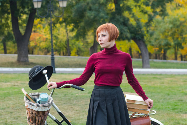junge Frau im Herbstpark liest Buch, schöne rothaarige Frau mit Fahrrad auf dem grünen Gras - Foto, Bild