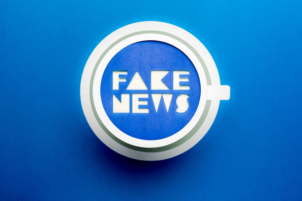 Fake News und Falschmeldung. Pappbecher mit Fake News Wörtern auf blauem Hintergrund. - Foto, Bild