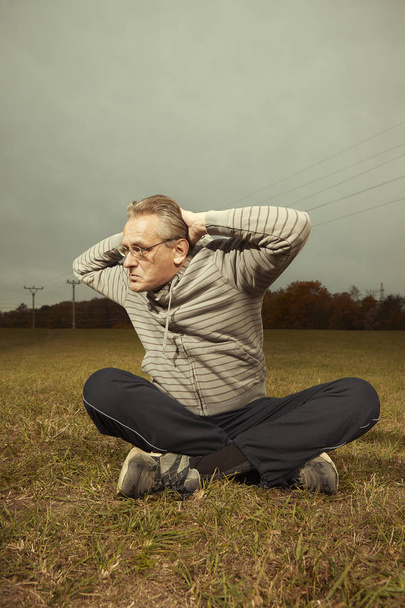 Aging older man exercising in sportsuit outdoor on meadow - Foto, Imagen