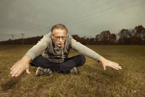 Aging older man exercising in sportsuit outdoor on meadow - Foto, afbeelding