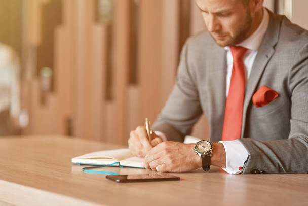 Write it down. Serious professional businessman sitting at the table and making notes while being involved in work - 写真・画像