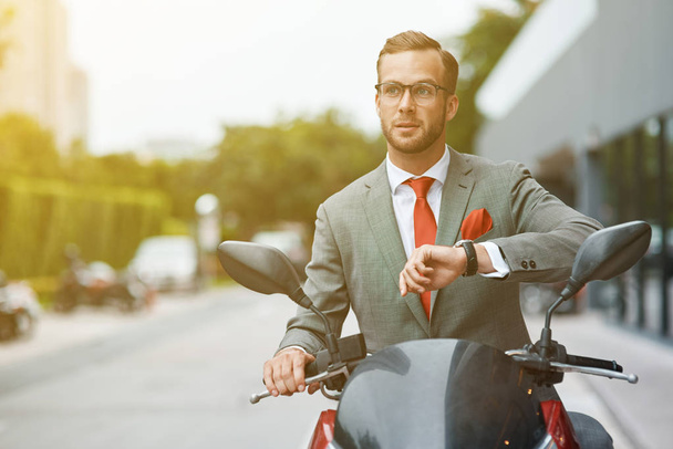 Lets speed up. Waist up of a professioanl confident young businessman checking time and sitting on the motorbike while going to work - Photo, Image