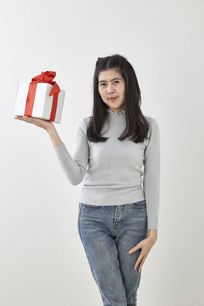junge asiatische Frau zeigen mit einem Geschenkkarton auf hellgrauem Wandhintergrund - Foto, Bild