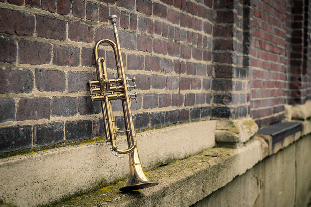 Oude roestige Jazz instrument trompet leunend tegen bakstenen muur gebouw buiten club - Foto, afbeelding