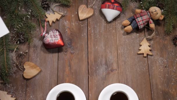 Vrolijk kerstfeest en gelukkig Nieuwjaar concept. Kopjes koffie geplaatst op houten achtergrond samen met spar boomtakken en heartshaped speelgoed. Witte opmerking komt in de buurt van cups - Video