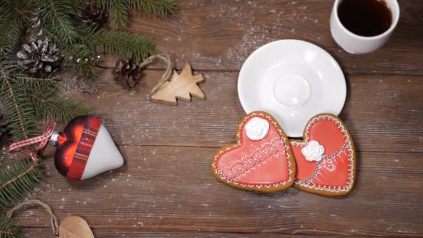 Vrolijk kerstfeest en gelukkig Nieuwjaar concept. Hart-vormige cookies, fir boomtakken en Kerstmis speelgoed zijn op houten achtergrond. Vrouwelijke hand zet een kopje koffie. - Video