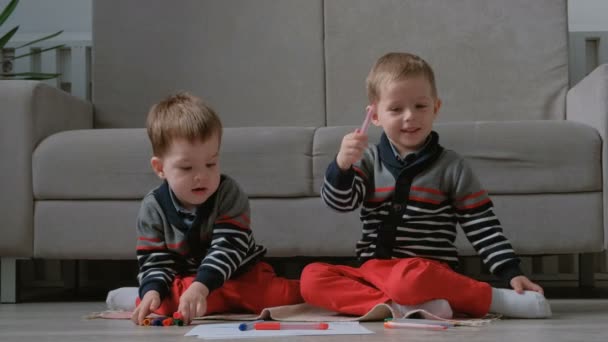 Two twin brothers toddlers draw together markers sitting on the floor. - Materiał filmowy, wideo