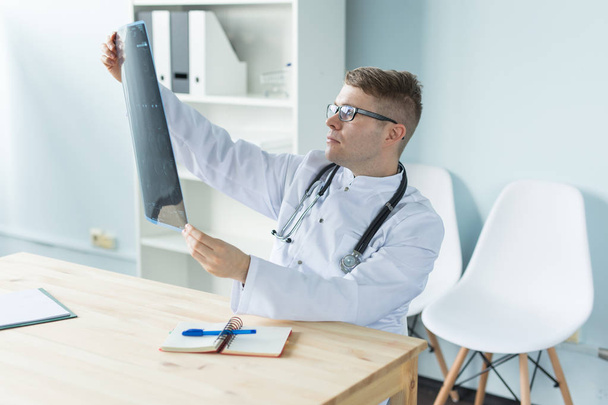 Zdravotní péče, lékařské a lidé koncept - lékař zkoumá rentgen sedí za stolem - Fotografie, Obrázek