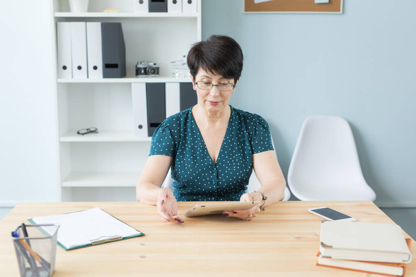 Geschäfts-, Büro- und Personalkonzept - hübsche Frau mittleren Alters konzentriert sich auf die Arbeit mit Tablets - Foto, Bild