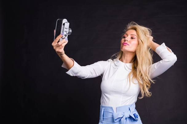 Fashion, leisure and beauty concept - Beautiful blond model in white shirt taking selfie over dark background - Photo, Image