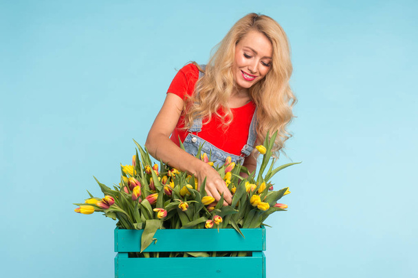 Floristika, dovolené, flower shop a lidé koncept - krásná blondýnka mladá oprava Kytice tulipánů na modrém pozadí. - Fotografie, Obrázek