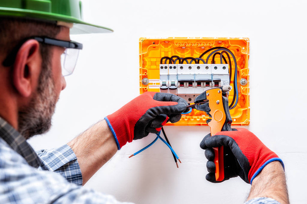 Technicien électricien avec casque, lunettes et gants mains protégées, travaille avec décapant dans un panneau électrique résidentiel
. - Photo, image