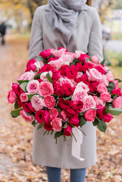 Big luxury bright bouquet in the hands of a cute girl. One hundred garden roses, varieties of David Austin. Three kinds of bright pink, scarlet and pastel colors. Autumn leaves in the Park. - Foto, Imagem