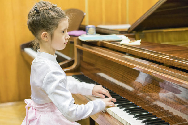 Una chica con un hermoso vestido toca en un piano de cola marrón
 - Foto, imagen
