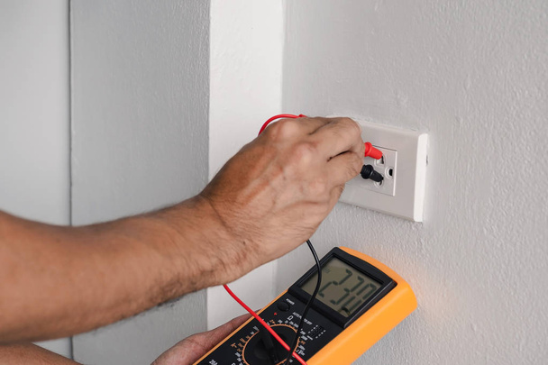 Elektricien is met behulp van een digitale meter voor het meten van de spanning op het stopcontact in op de muur. - Foto, afbeelding