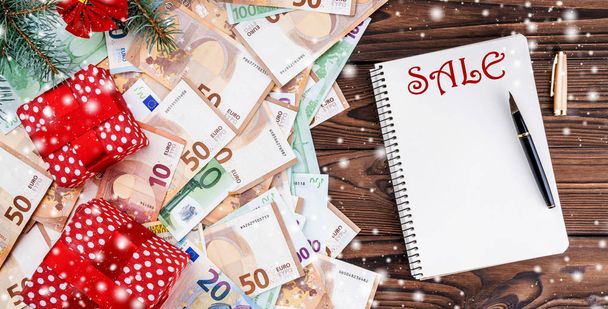 European money of different value on wood background. Gifts under fir branches. Space for text. Top view. Effect snowflakes. - Zdjęcie, obraz