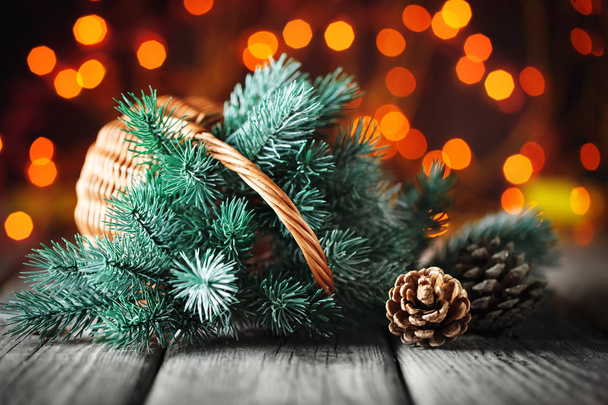 Feliz Navidad y feliz año nuevo. Cesta con ramas del árbol de Navidad sobre una mesa de madera sobre el fondo de una guirnalda
. - Foto, Imagen