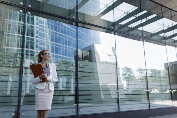 The young woman in gray office dress holds in hand folder with documents. Businesswoman standing next to the business center - Foto, Imagem