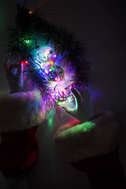 クリスマス ライトのモミの枝の近くのボールを配置するサンタ クロースの腕の上から見る - 写真・画像