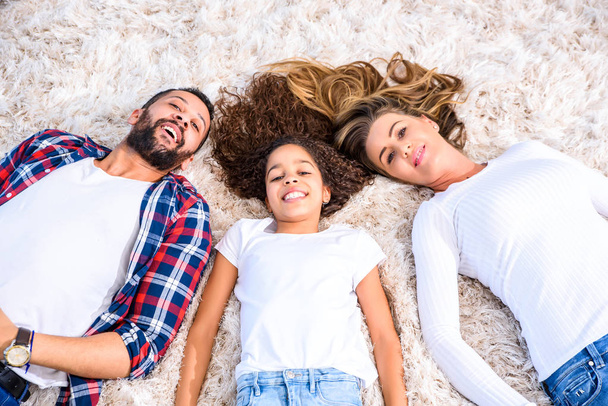 Young parents and their daughter laying on the carpet - Φωτογραφία, εικόνα