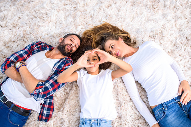 Young parents and their daughter laying on the carpet - 写真・画像