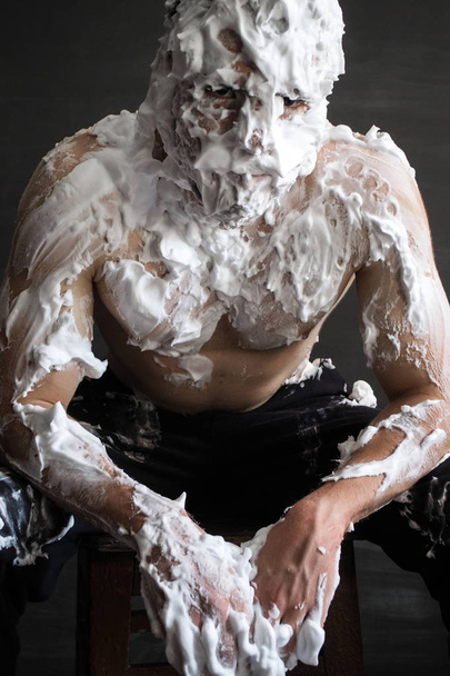 photo portrait of a muscular guy smeared with shaving foam sitting and leaning forward - Fotografie, Obrázek