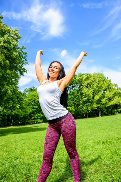 Красивая молодая спортивная девушка, счастливо поднимающая руки на поле в парке
 - Фото, изображение
