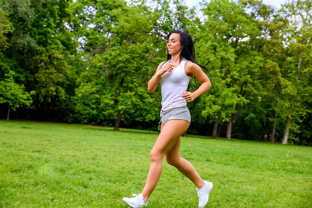A beautiful young sporty girl running on a field in a park while wearing shorts and a top - Foto, imagen