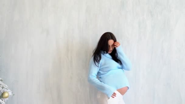 une femme enceinte dans un pull bleu se tient aux murs blancs
 - Séquence, vidéo
