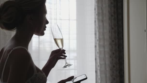 Silhouette of a pretty girl with a phone against the window - Filmagem, Vídeo
