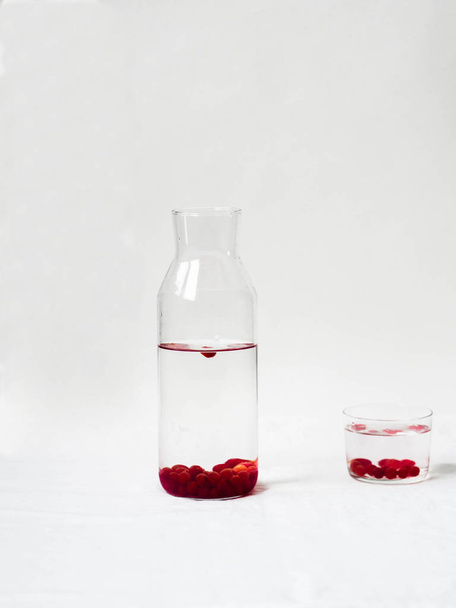 Water with red berries viburnum in a glass jug on a white background. Copy space - Φωτογραφία, εικόνα