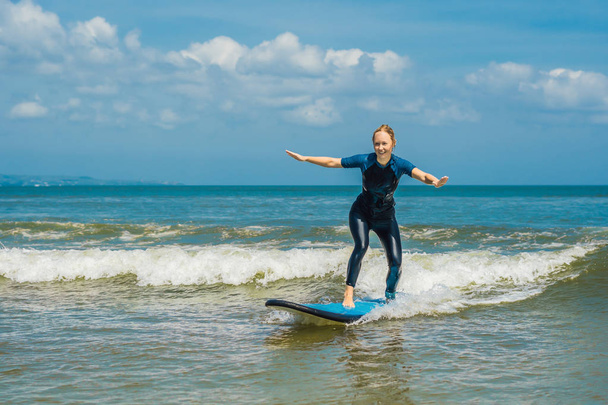 Young woman learning surfing on sea water with blue beginner surf board. - Foto, Imagem