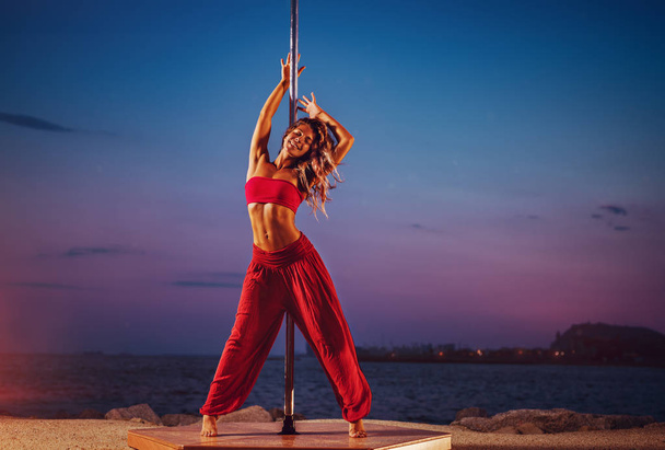 Young woman pole dancing on sea and sky background at twilight - Zdjęcie, obraz