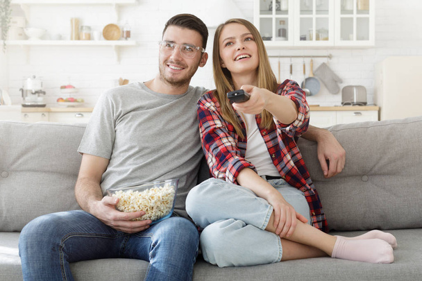 Young happy couple watching tv. Cheerful family sitting on sofa with popcorn bowl  - Fotografie, Obrázek
