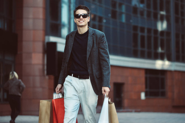 Sérieux mec cool avec des lunettes de soleil et des sacs en papier marchant dans la rue
. - Photo, image
