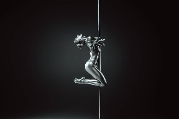Young woman pole dancing. Silver body paint and toning. Dramatic colors. - Fotó, kép