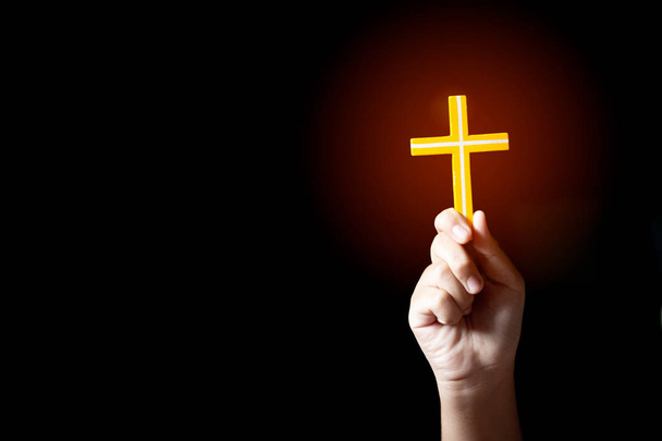 Mão humana segurando e levantar da cruz cristã com fundo preto claro
 - Foto, Imagem